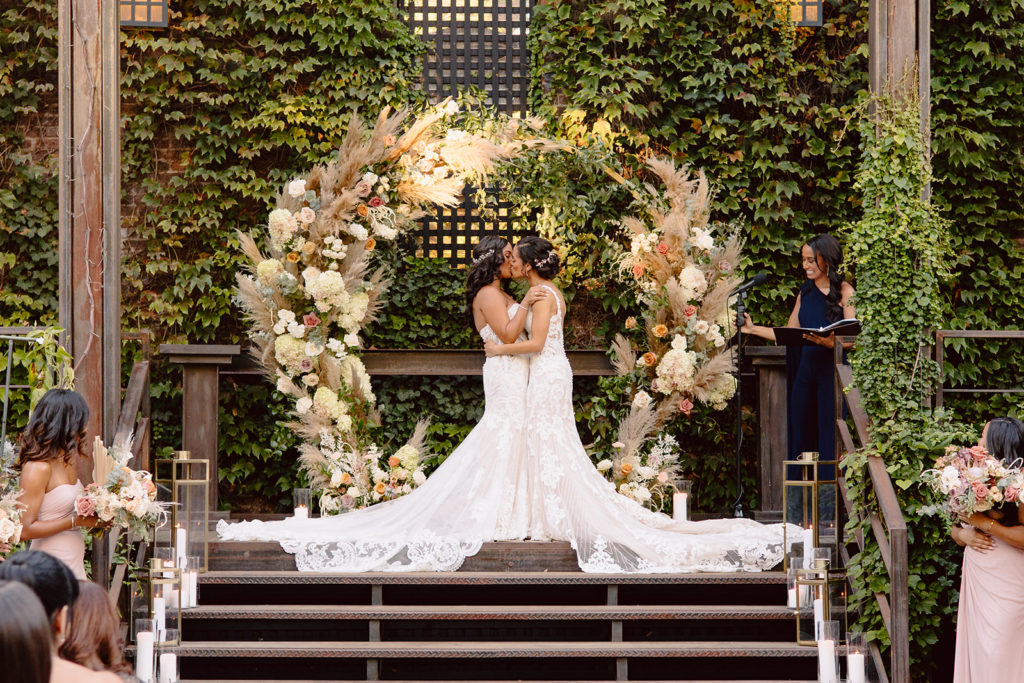 industrial meets boho wedding ceremony with a circle arch covered in pampas grass, hydrangea and roses