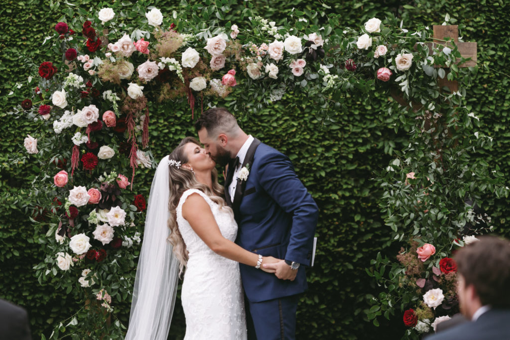 bride and groom saying i do under a floral arch with hanging amaranthus