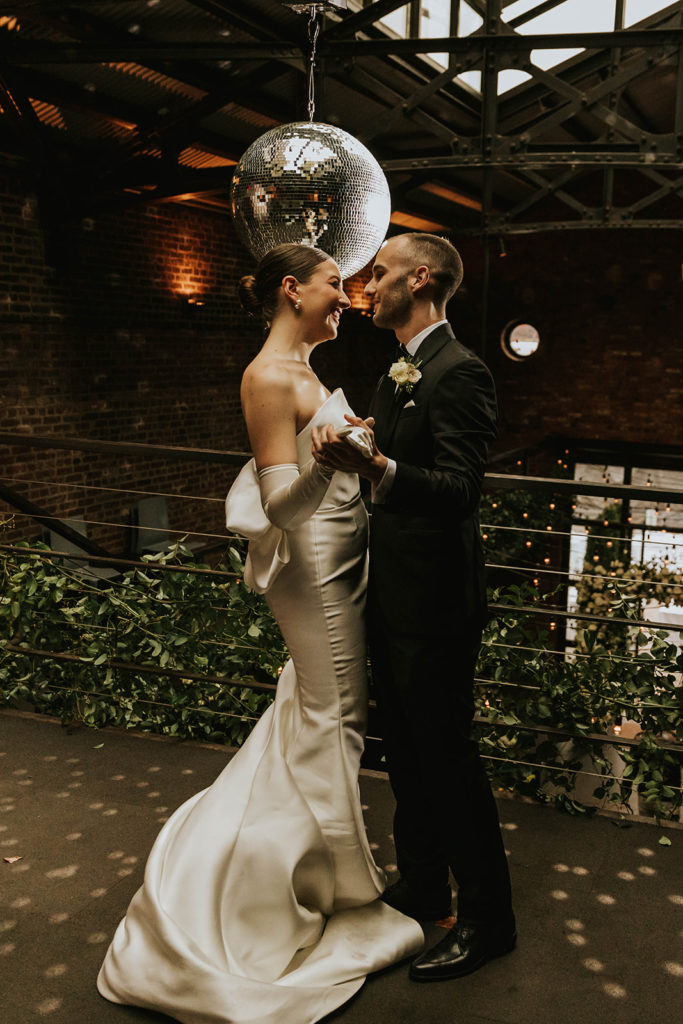 bride and groom dancing with disco ball and hanging greenery behind them