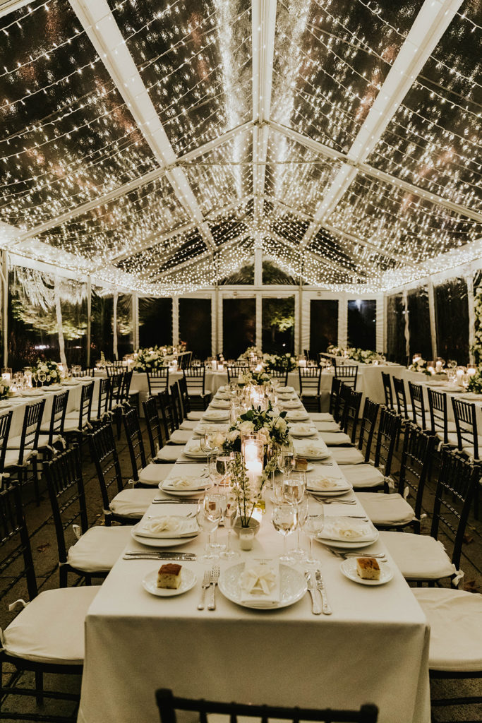 twinkly lights covering a wedding reception tent. Tables dressed with floral arrangements and candles.