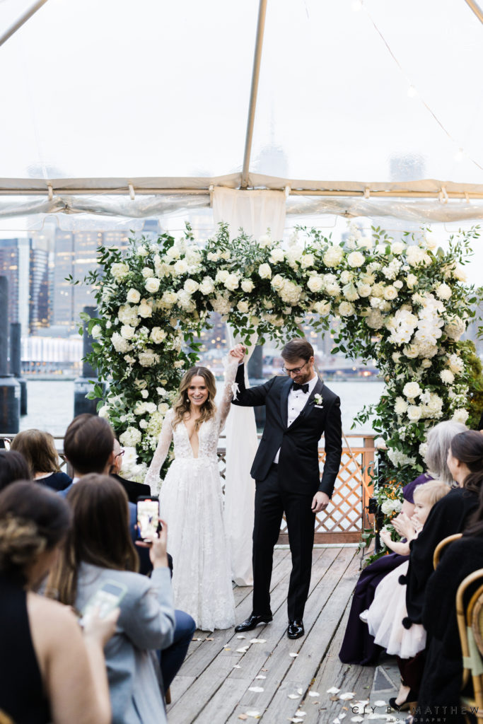 Bride and Groom Celebrating after their first kiss under a chic white and green floral arch with hydrangea roses and orchids